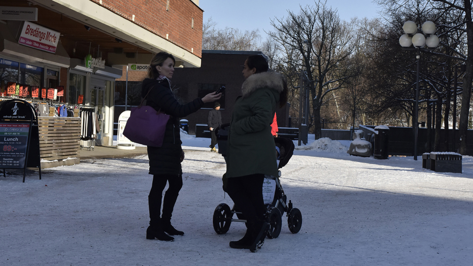 En kvinna intervjuar en kvinna med barnvagn på ett snöigt torg.